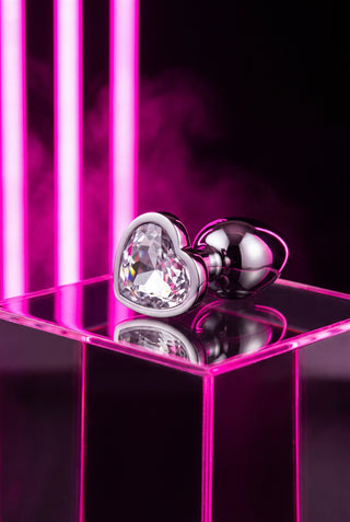 PRETTY SECRET Ice — plug de acero pulido con corazón de cristal transparente sobre podio de acrílico con neón rosa